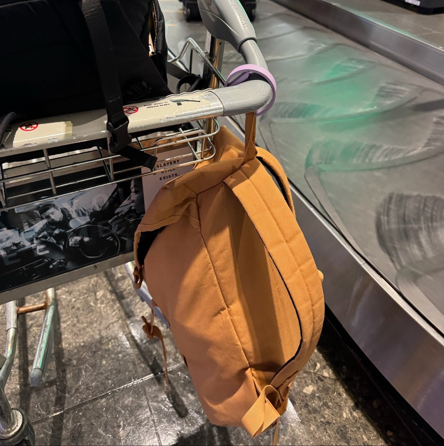 Yellow bag hanging on a luggage cart at an airport baggage claim area.